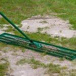 Man uses a lawn rake to put a layer of sand on the lawn. The topdressing levels out uneven parts and helps to ventilate the lawn.