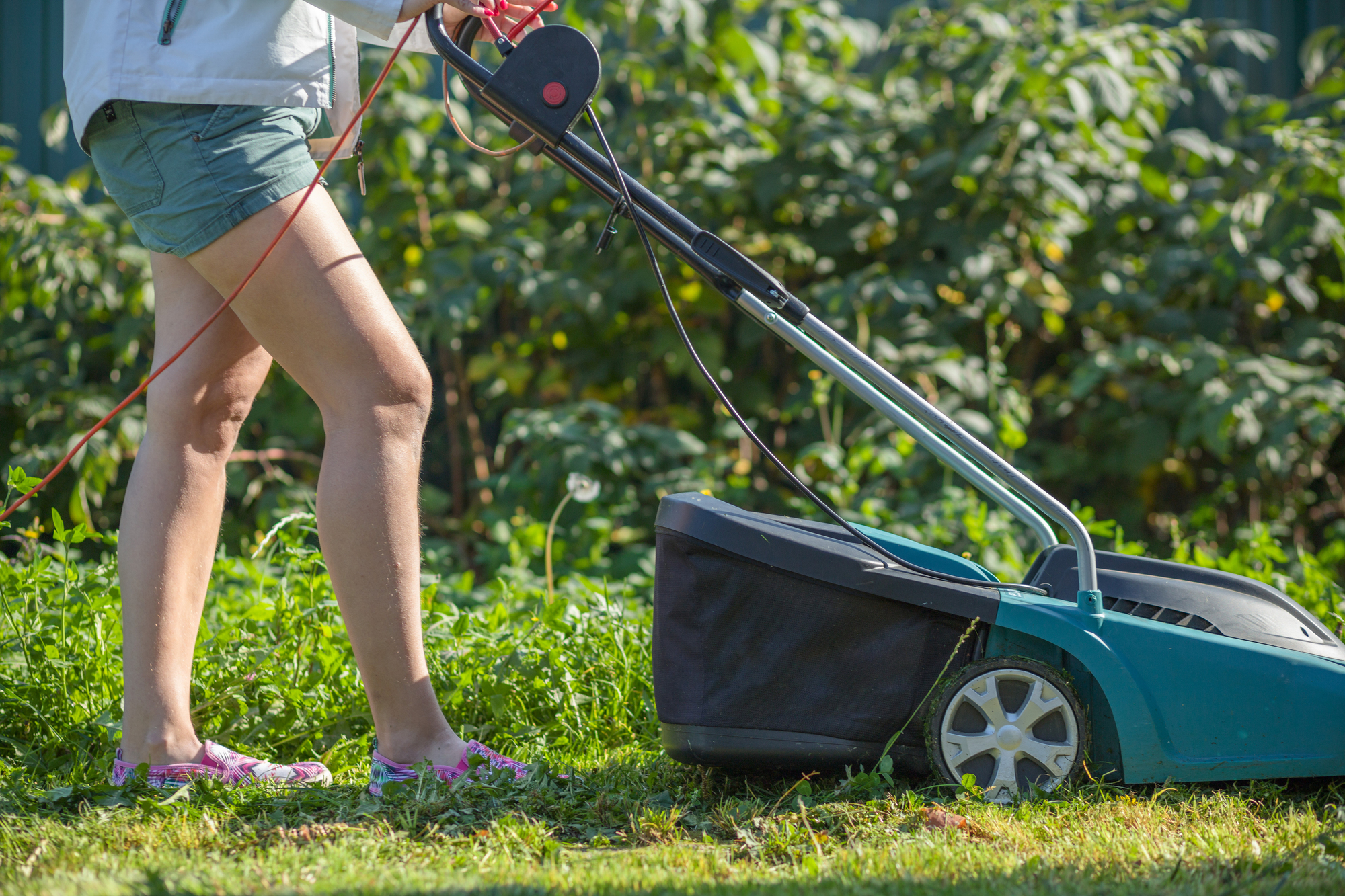 Woman cuts the lawn with an electric mower