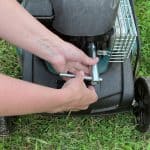 Changing replacing lawn mower spark plug, landscape equipment repair service, process of unscrewing spark plug.
